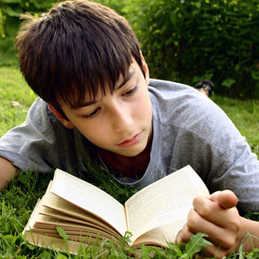 Boy laying in grass reading book